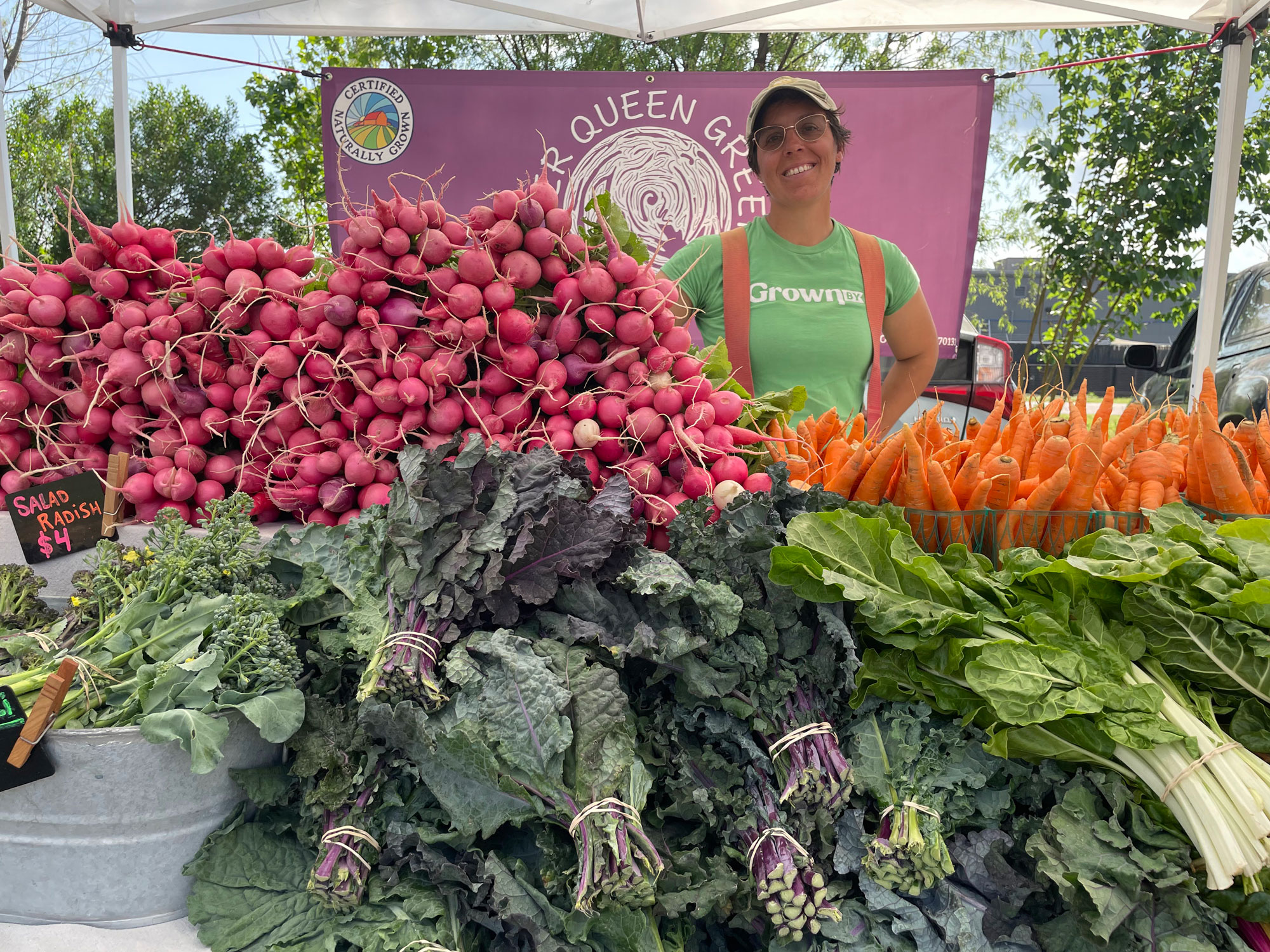 Co-owner Cheryl Nunes standing behind produce at the River Queen Greens farmers market stand