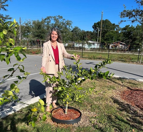 A woman gesturing at a small tree in front of her